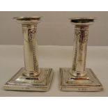 A pair of hallmarked silver table candlesticks, the tubular stems with husk and tie decoration on