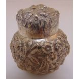 A white metal tea caddy with domed pull off cover profusely chased with leaves and flowers, approx