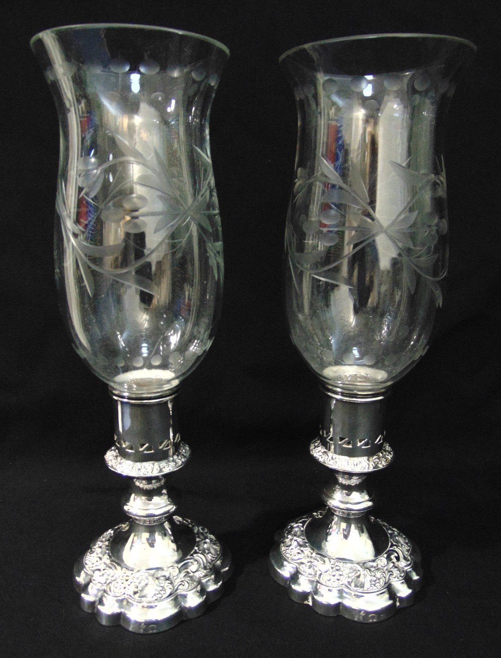 A pair of engraved glass storm lanterns with silver plated bases of circular form with scroll chased