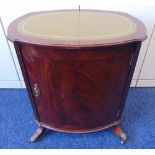 A mahogany oval cabinet with tooled leather top on four claw feet and hinged door with brass handle,