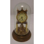 A brass anniversary mantle clock with circular white dial and Roman numerals supported by two