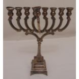 A white metal Menorah, the scrolling arms on fluted leaf chased stem and stepped square base on four