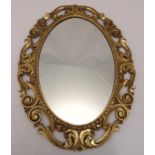 An oval gilded wooden wall mirror, pierced and carved with scrolls and stylised leaves, 77 x 57.5cm