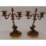 A pair of two branch gilded metal candelabra of organic form supported by putti on shaped oval