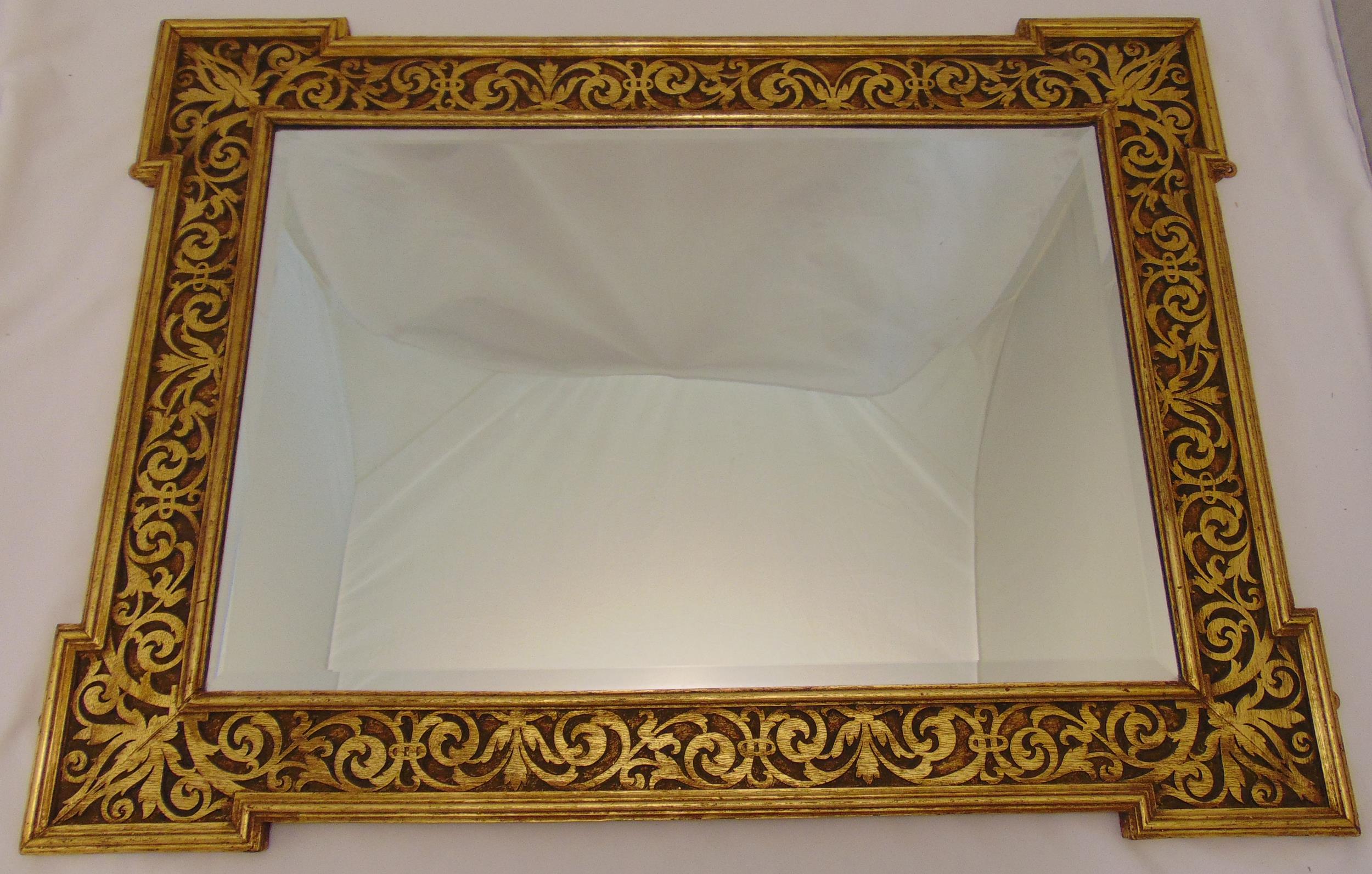 A shaped rectangular bevelled edge wall mirror mounted in a carved low relief gilded wooden frame,