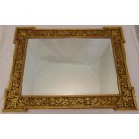 A shaped rectangular bevelled edge wall mirror mounted in a carved low relief gilded wooden frame,