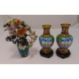 A pair of oriental cloisonné vases on carved wooden stands and a vase with simulated flowers made of