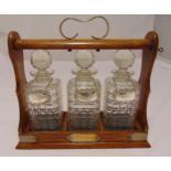 A late Victorian three bottle cut glass tantalus in oak frame with scroll handle and three