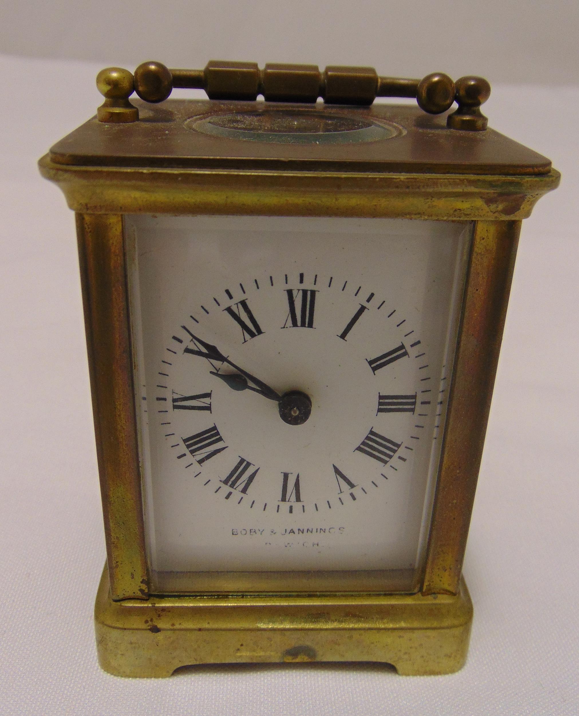 A miniature brass carriage clock of customary form with Roman numerals, swing handle on four bracket