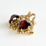 A late 20th century 9ct gold garnet and split pearl double-heart brooch, with ribbon surround,