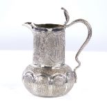 A small early 20th century Indian unmarked silver cream jug, allover engraved decoration with