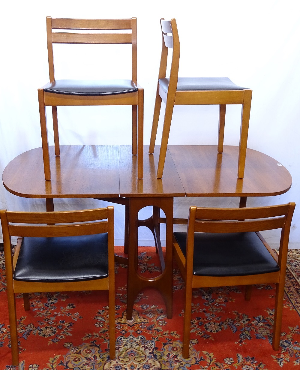 A mid-century teak dining room suite, comprising a bow-end drop leaf dining table, 4 matching chairs
