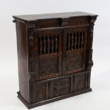 A small 19th century carved and panelled oak wall-hanging cupboard, with spindled panelled doors,