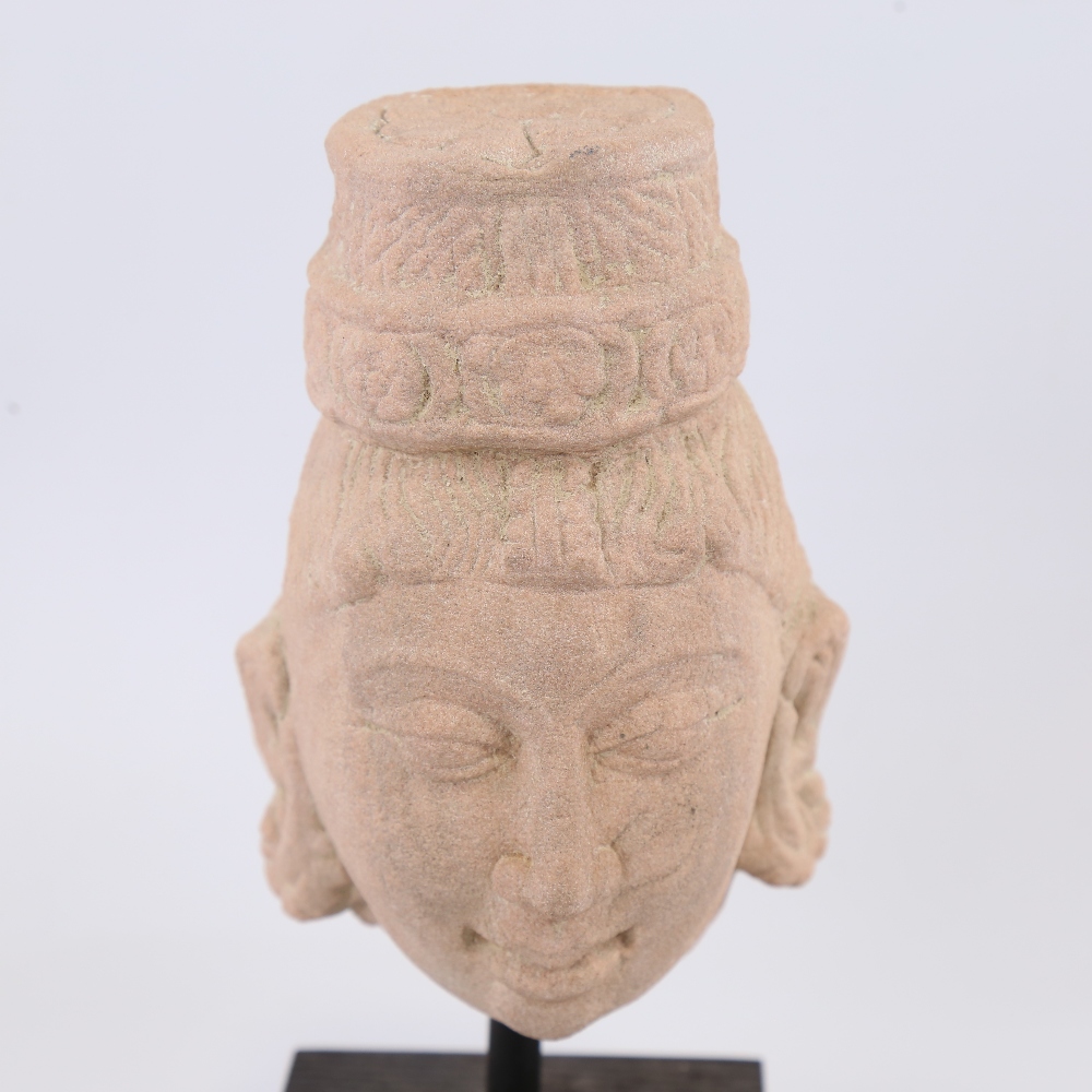 An Indian carved red stone head of a goddess, modern block plinth, overall height 23cm Probably a