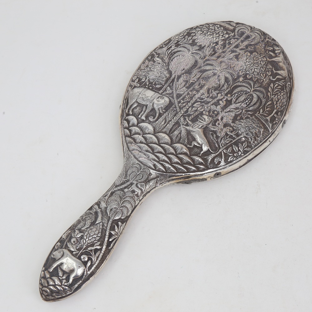 An unmarked Indian silver dressing table hand mirror, allover relief embossed animal and jungle