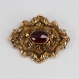 A Victorian unmarked gold cabochon garnet brooch, relief foliate border with textured ground and