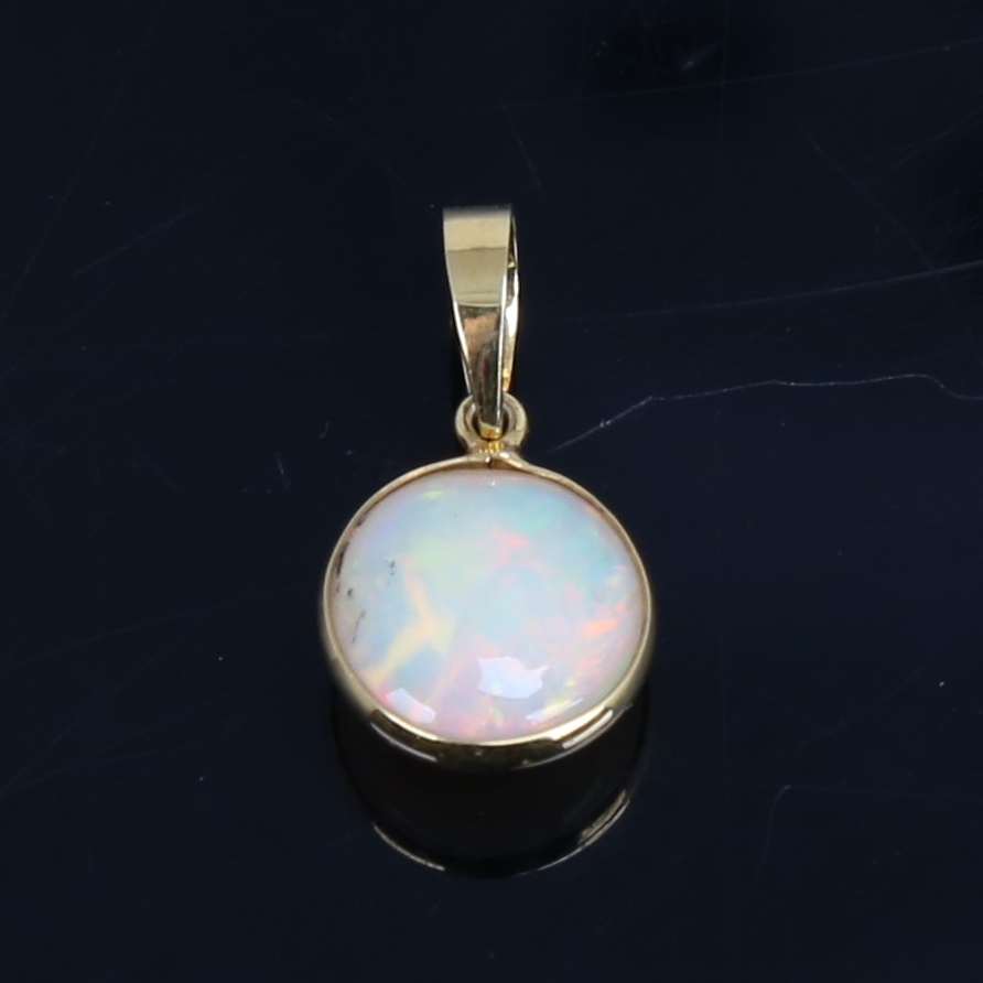 A modern handmade unmarked gold Ethiopian opal pendant, set with round cabochon opal, settings