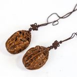 A pair of Chinese relief carved nut pendants on cords