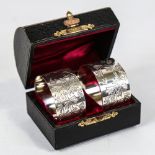 A cased pair of Edwardian silver napkin rings, cylindrical form with engraved floral decoration,