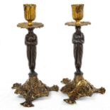 A pair of patinated and gilded bronze candlesticks, supported by Classical figures, height 22cm