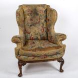 A Georgian wingback armchair, with out-scrolled arms and needlepoint upholstery, raised on carved