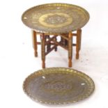 A Middle Eastern folding table, with a circular brass and white metal embossed top, and similar oval