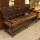 An 18th century joined oak settle, with a carved and fielded panelled back, on turned legs,