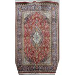 A large red ground Persian Kashan wool rug, all over floral design with blue ground border, 295cm