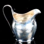 A George III silver helmet-shaped cream jug, engraved foliate decoration with reeded rim, indistinct