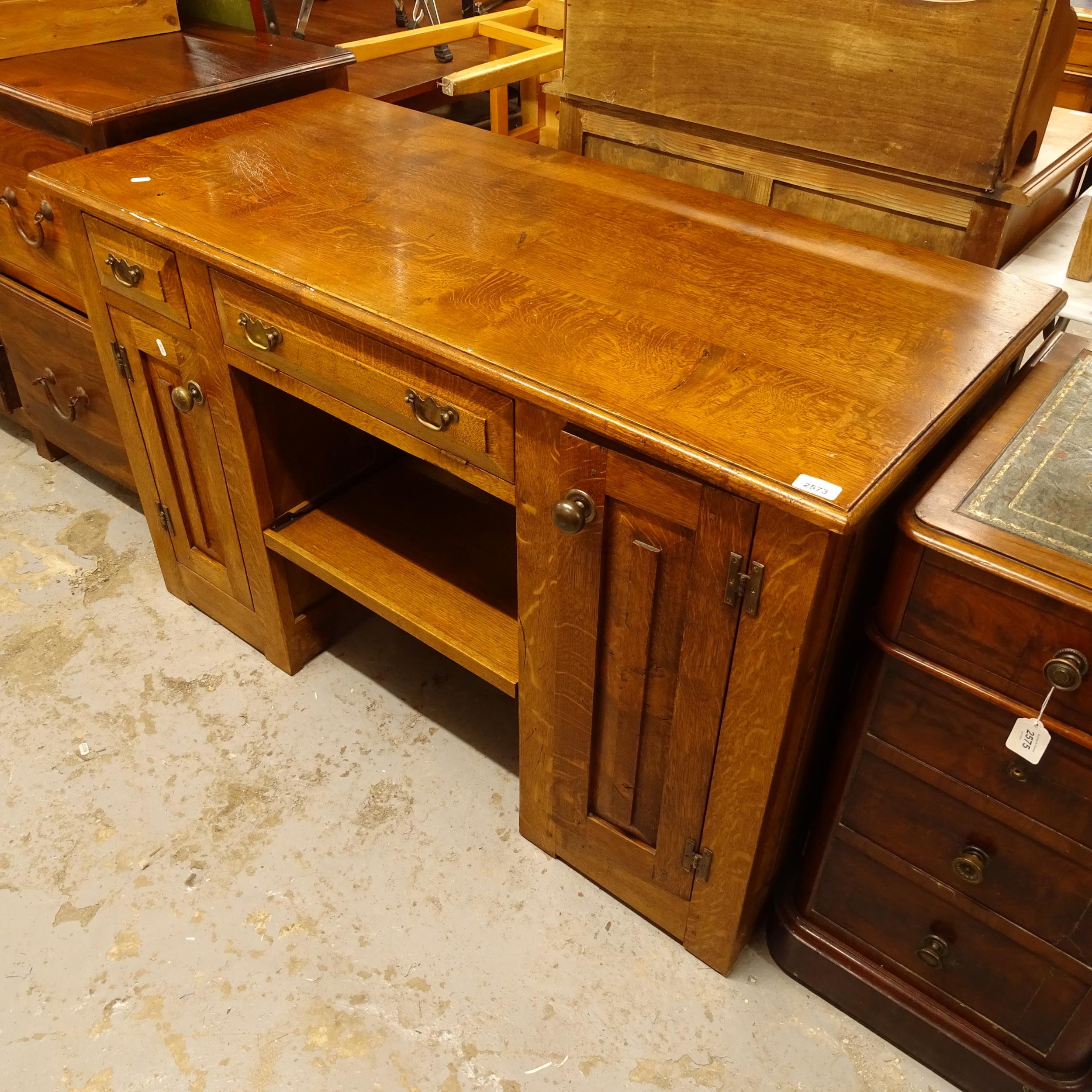 An Arts and Crafts design oak desk, with drawers and panelled cupboards, W127cm, H80cm, D57cm