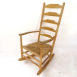 A mid-century Arts and Crafts Cotswold School style ladder-back rocking chair, in ash, with rush