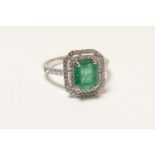 Emerald and diamond cluster ring, in 18ct white gold, the central emerald of approx. 1ct, bordered
