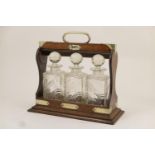 George V oak three bottle tantalus, having plated brass mounts and three slice cut decanters, with