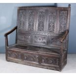 An Old Panelled "Black Oak" Settle, the high five panel back carved with leafage, with triple