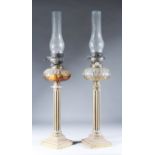 A Pair of Late Victorian Brass Table Oil Lamps, the bulbous glass reservoirs with oval panel