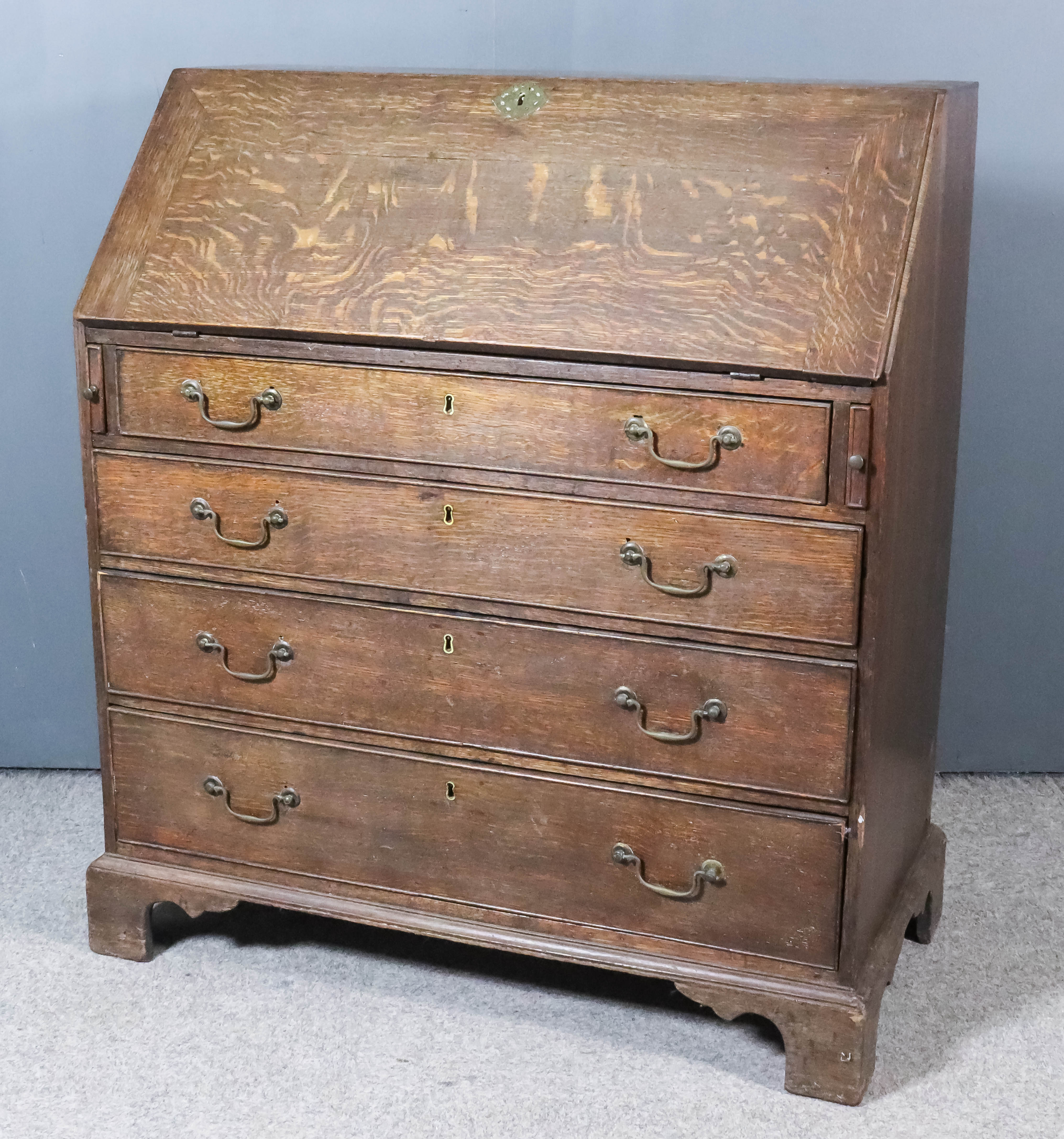 A George III Oak Bureau, the slope enclosing pigeon holes, small central cupboard and six small