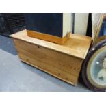 A STRIPPED WOODEN BEDDING BOX, WITH END HANDLES AND HINGED LID, RAISED ON CASTORS