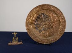 AN INTER-WAR YEARS STAMPED BRASS WALL PLAQUE, and a SMALL BRASS RELIGIOUS DEVOTIONAL ORNAMENT (2)