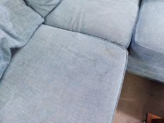 A LARGE 'L' SHAPED SETTEE COVERED IN BLUE FABRIC ON BUN FEET