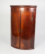 GEORGE III FIGURED MAHOGANY BOW FRONTED CORNER CUPBOARD, of typical form with dentil moulded