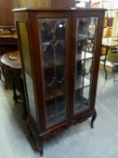 A CARVED MAHOGANY DWARF DISPLAY CABINET ENCLOSED BY TWO GLAZED DOORS, WITH CARVED APRON AND CABRIOLE