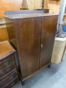 AN OAK TWO DOOR MILLINERY CABINET ENCLOSING TWO SHELVES AND A DRAWER, ON STUMP CABRIOLE SUPPORTS,