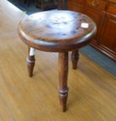 A SMALL CIRCULAR HARDWOOD MILKING STOOL ON THREE LEGS