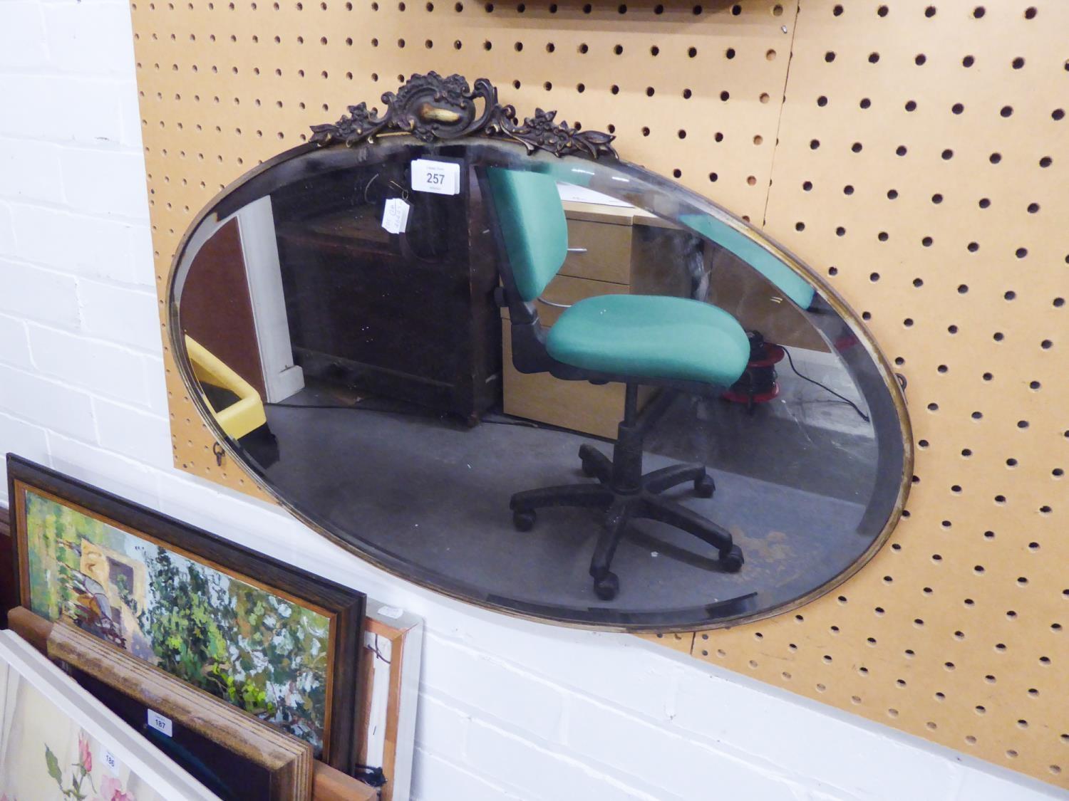 AN OVAL BEVELLED EDGE WALL MIRROR, IN SILVERED METAL FRAME WITH ROCOCO PEDIMENT