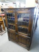 JACOBEAN STYLE OAK BOOKCASE, WITH TWO LEAD LIGHT DOORS OVER A CUPBOARD WITH TWO LINEN FOLD CARVED