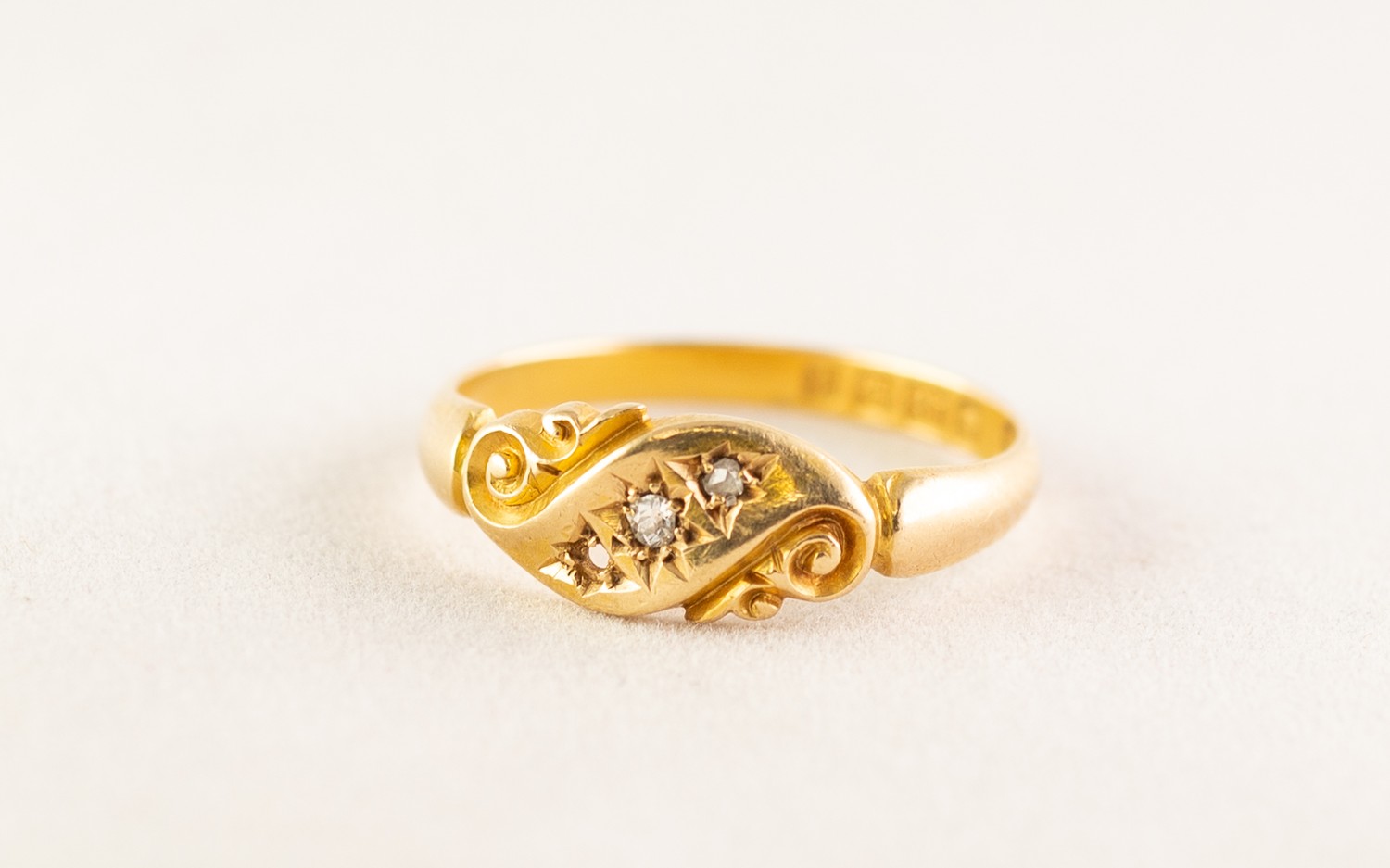 AN EDWARDIAN 18ct GOLD RING, with two tiny rose diamonds in a scroll pattern cross setting (one