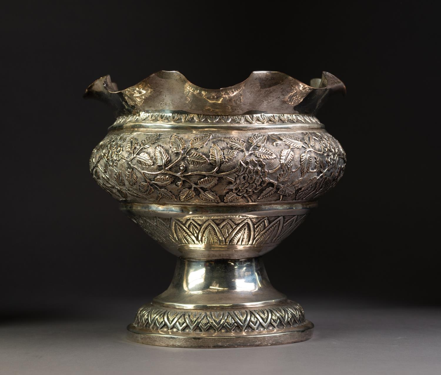 EASTERN SILVER COLOURED METAL PEDESTAL DEEP BOWL, with plain wavy top, the bulbous body repousse