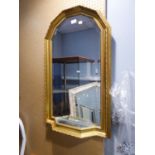 A GILT FRAME ARCH TOPPED WALL MIRROR, WITH SMALL SHELF BELOW WITH MIRROR GLASS TOP