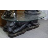 AN OVAL GLASS TOPPED COFFEE TABLE, ON LARGE BLACK FIBREGLASS BASE IN THE FORM OF A RECLINING