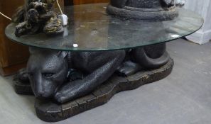 AN OVAL GLASS TOPPED COFFEE TABLE, ON LARGE BLACK FIBREGLASS BASE IN THE FORM OF A RECLINING